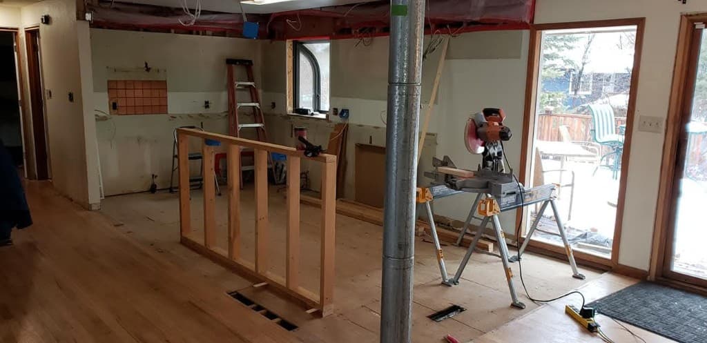Full gut kitchen remodel demolition in a Fort Collins home showing exposed studs, framing for a new island wall, and stripped-down subfloor before construction
